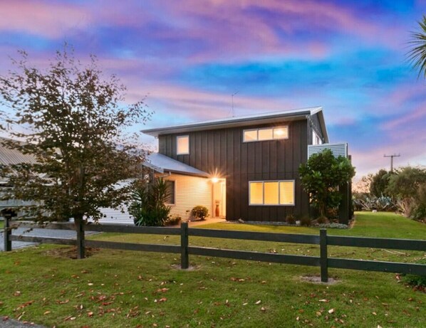 A modern two-story house with a dark exterior, a well-maintained lawn, and a wooden fence in the foreground. - 5BR-Sleeps 12, 50m to Lake Near CBD & Attractions (Rotorua)