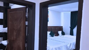 A hotel room with two beds, a wooden wardrobe, and a bathroom visible through an open door. -  شقق لمسات الخير للوحدات السكنية - شقق مخدومة (Jeddah)