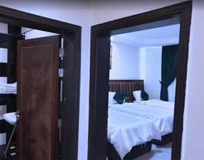 A hotel room with two beds, a wooden wardrobe, and a bathroom visible through an open door. -  شقق لمسات الخير للوحدات السكنية - شقق مخدومة (Jeddah)