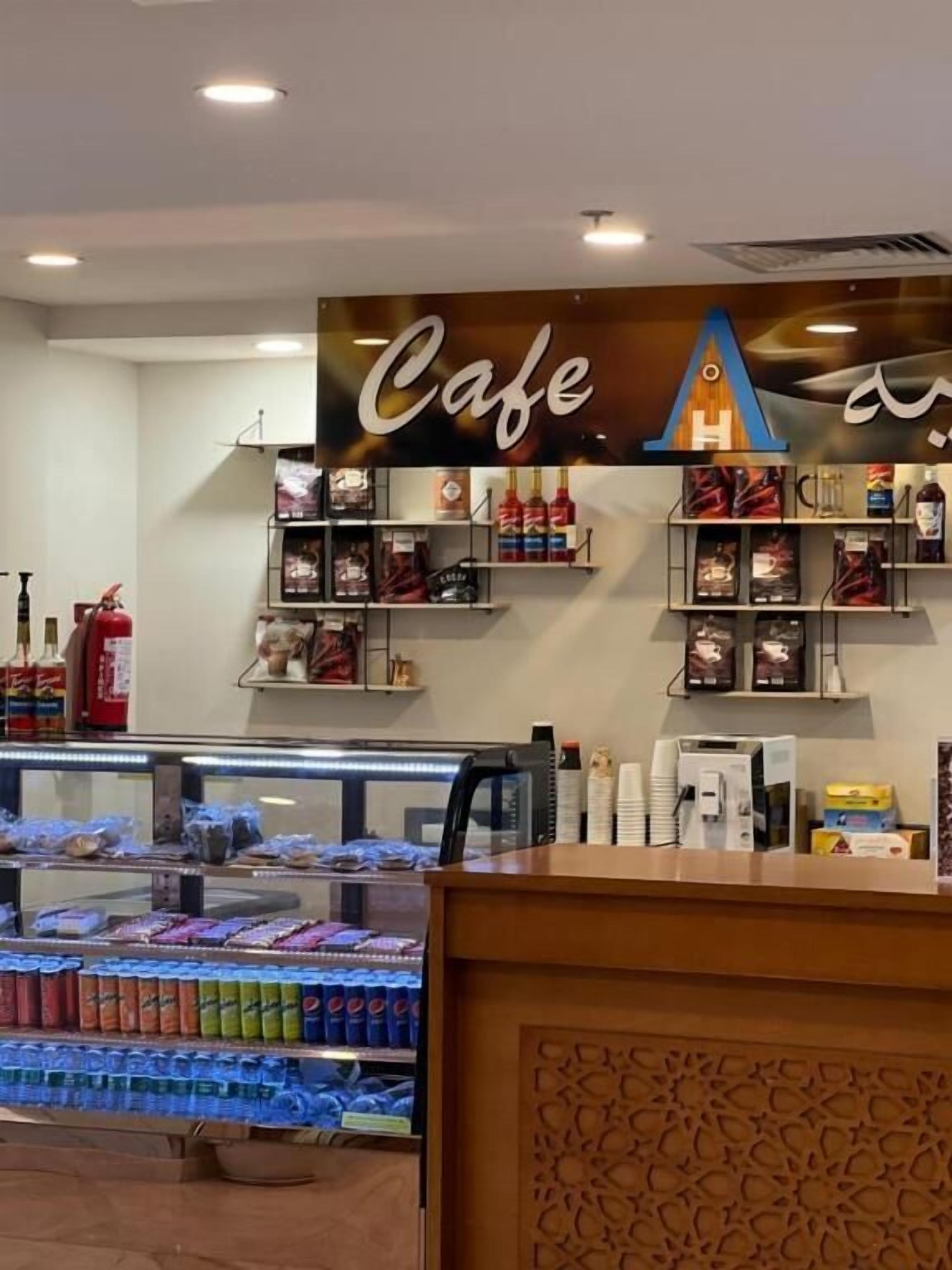 A cafe with a display case of snacks and beverages, shelves with coffee and tea products, and a fire extinguisher on the wall.
