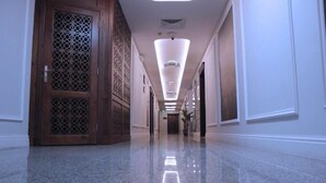A long, polished hallway with a wooden door on the left and a bright, modern light fixture overhead. -  شقق لمسات الخير للوحدات السكنية - شقق مخدومة (Jeddah)