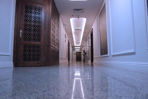 A long, polished hallway with a wooden door on the left and a bright, modern light fixture overhead.