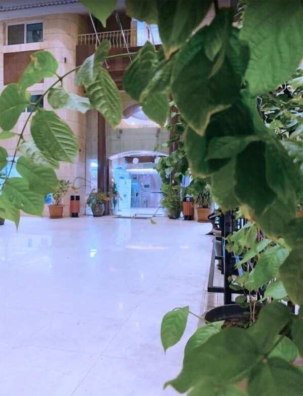 A spacious lobby with a high ceiling, potted plants, and a central area with a counter and seating. -  شقق لمسات الخير للوحدات السكنية - شقق مخدومة (Jeddah)