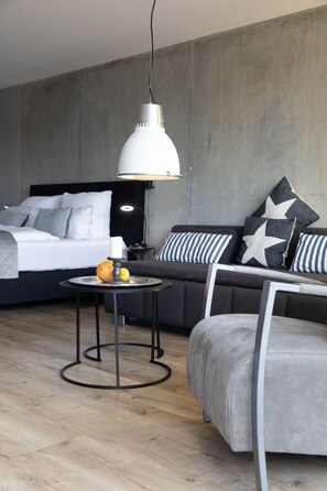 Ein modernes Schlafzimmer mit einem Bett, einem Schlafsofa, einem runden Tisch mit Obst und einer Pendelleuchte.