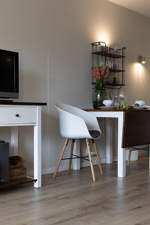 Eine moderne Küche mit einem weißen Esstisch, einem weißen Stuhl, einem Fernseher und einem Regal mit Gläsern und Blumen.