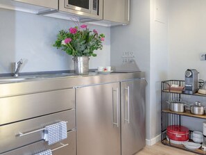 A modern kitchen with stainless steel cabinets, a microwave, and a vase with flowers on the counter. - Loft - Neu ab 15.01.2024 - Cityloft- Modernes Appartement für 2 Personen in Zentraler Lage (Sylt)