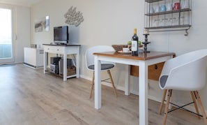 A modern kitchen with a wooden table, white chairs, a television, and a wine bottle. - Loft - Neu ab 15.01.2024 - Cityloft- Modernes Appartement für 2 Personen in Zentraler Lage (Sylt)