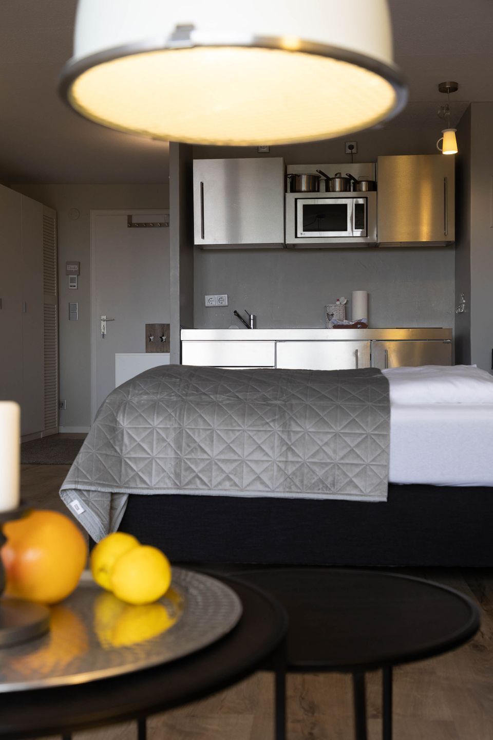 A modern bedroom with a bed, bedside table, and a view of a kitchenette.