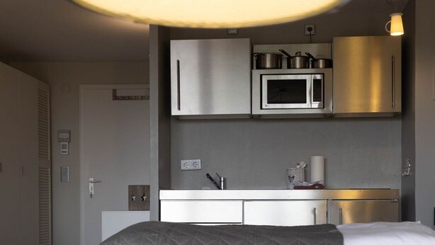 A modern bedroom with a bed, bedside table, and a view of a kitchenette. - Loft - Neu ab 15.01.2024 - Cityloft- Modernes Appartement für 2 Personen in Zentraler Lage (Sylt)