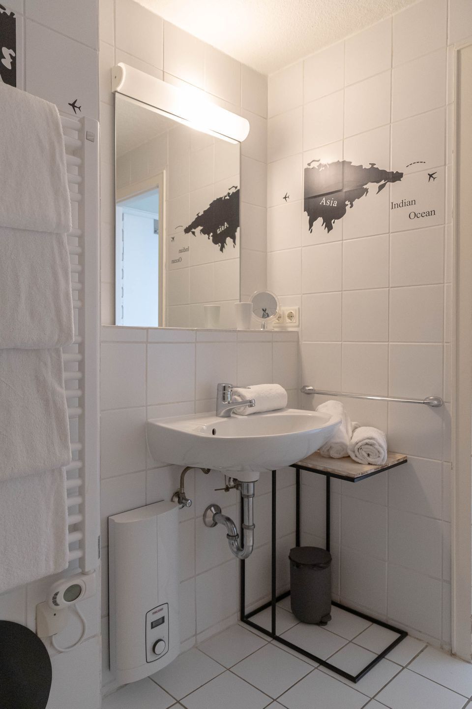 A bathroom with a white sink, mirror, towel rack, and a map of Asia on the wall.