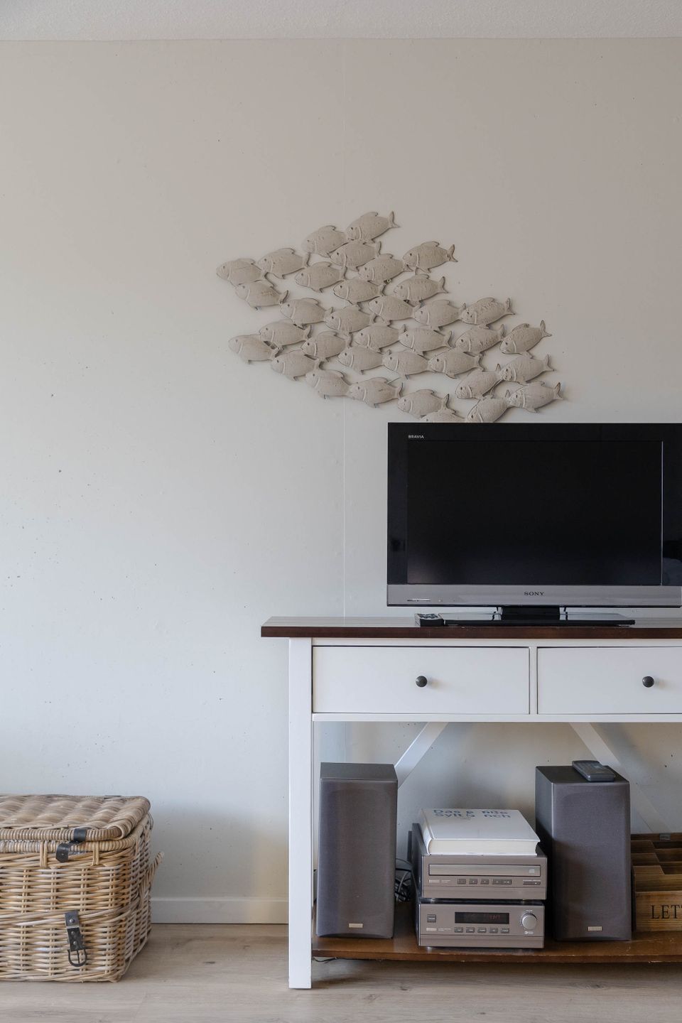 Un téléviseur à écran plat posé sur un meuble télé blanc, avec un tableau décoratif représentant des poissons accroché au mur au-dessus.