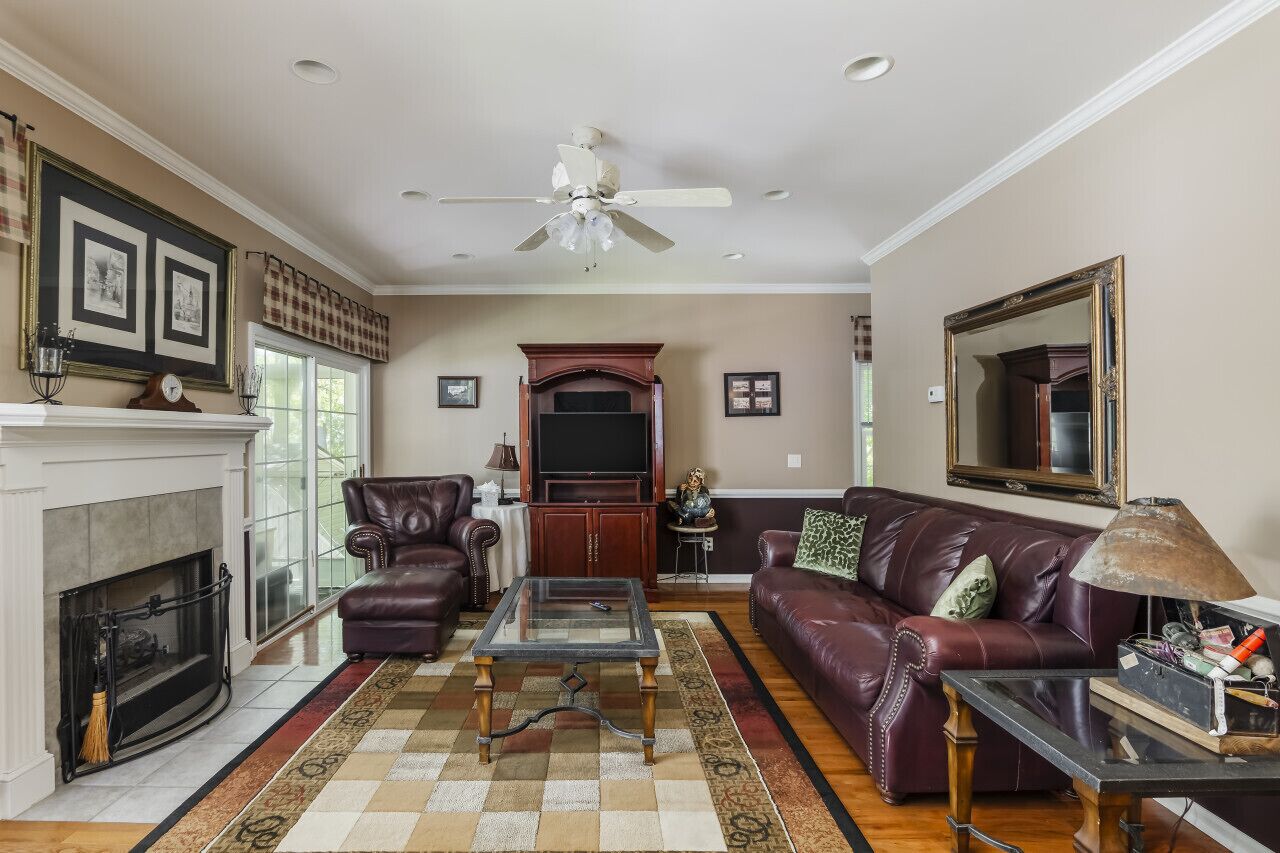 A living room with a fireplace, leather furniture, a television, and a ceiling fan.