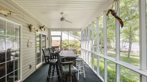 Eine überdachte Veranda mit Esstisch und Stühlen, großen Fenstern und einem Deckenventilator.