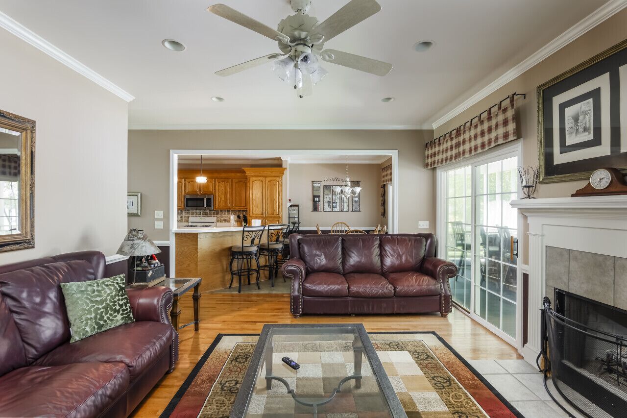 A living room with a fireplace, a ceiling fan, and a kitchen in the background.