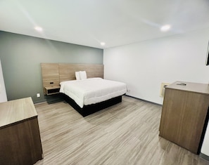 A modern hotel room with a bed, bedside tables, a desk, and a wardrobe. - Rodeway Inn Mineola (Mineola)