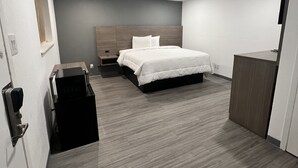 A modern hotel room with a large bed, a wooden headboard, a desk, and a wardrobe. - Rodeway Inn Mineola (Mineola)