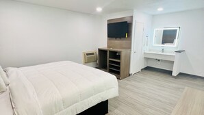 A modern hotel room with a large bed, a TV mounted on the wall, a vanity with a mirror, and a small seating area. - Rodeway Inn Mineola (Mineola)