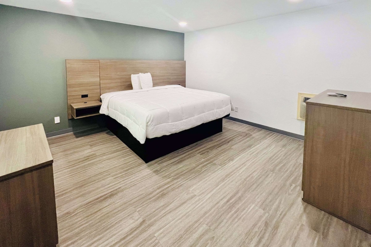 A modern hotel room with a bed, a nightstand, and a wooden dresser.