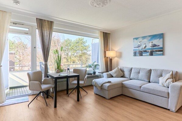A modern living room with a sofa, chairs, a table, and a painting of seagulls.