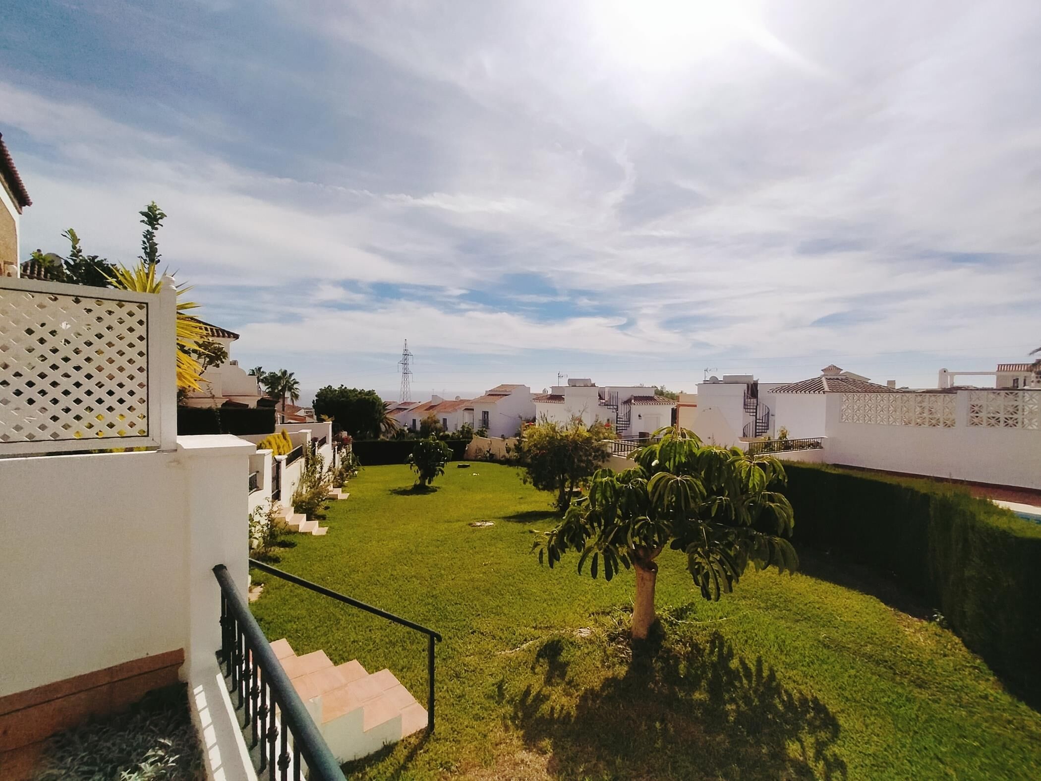 A residential area with a well-maintained lawn, a staircase leading to a balcony, and a view of neighboring houses.