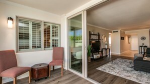Un salon doté d’une grande porte-fenêtre coulissante donnant sur un balcon, d’une cheminée et d’un coin salon avec deux fauteuils et un petit pouf.