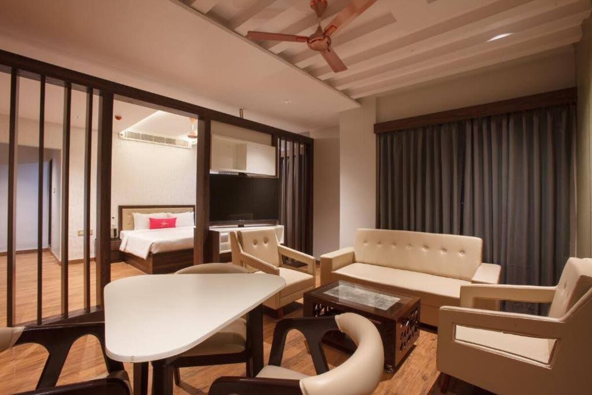 A hotel room with a sofa, chairs, a TV, a bed, and a ceiling fan.