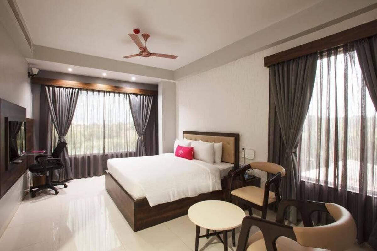 Una habitación de hotel con cama, escritorio, silla, mesita y ventilador de techo.