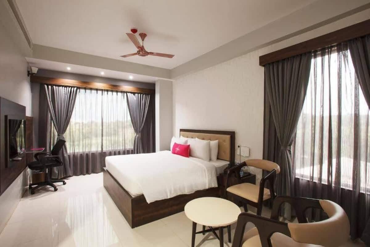 Une chambre d’hôtel équipée d’un lit, d’un bureau, d’une chaise, d’une petite table et d’un ventilateur de plafond.