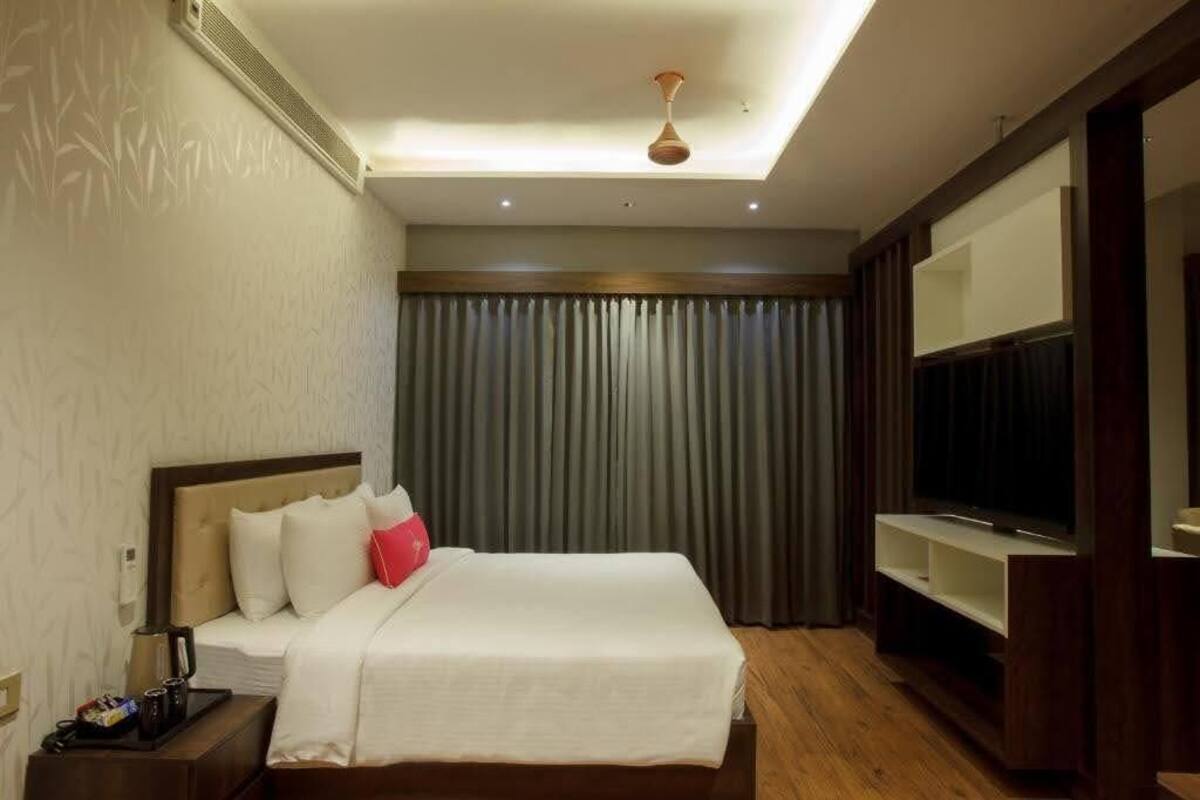 Una habitación de hotel con cama, televisor, mesita de noche y luz en el techo.
