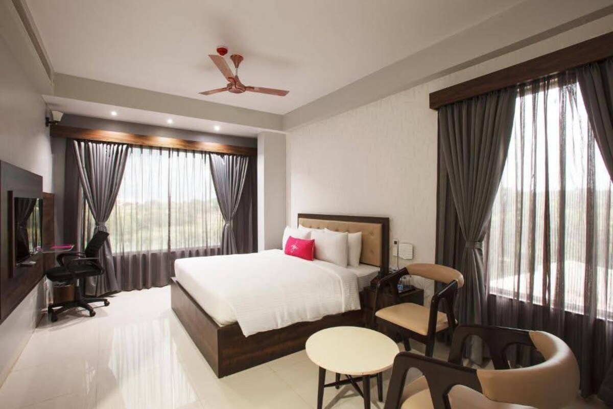 A hotel room with a bed, a desk, a chair, a small table, and a ceiling fan.