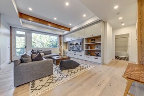 A modern living room with a grey sofa, a coffee table, and a TV. There is a wooden bench and a bookshelf with decorative items.