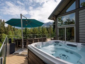 A hot tub on a wooden deck with a mountain view, a large umbrella, and outdoor seating.