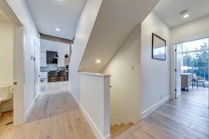 A modern interior with a kitchen, dining area, and a staircase leading to a balcony. - Nighthawk 3343 - Private Hot Tub, Mountain Views, Above Whistler Golf Course (Whistler)
