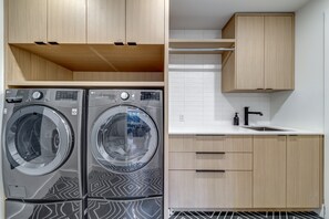 A modern laundry room with two front-loading washing machines, a sink, and wooden cabinets.
