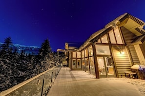 A modern building with large windows, a covered outdoor area, and a view of snow-covered trees.