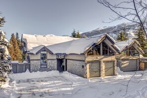 A snow-covered lodge with a stone facade, a garage, and a mountain backdrop. - Nighthawk 3343 - Private Hot Tub, Mountain Views, Above Whistler Golf Course (Whistler)