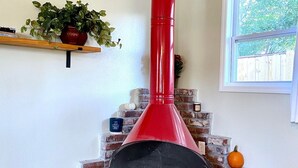 A brick fireplace with a red chimney, a window with a view of greenery, and a shelf with a plant.