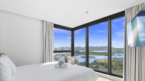 Ein modernes Schlafzimmer mit einem großen Bett, Blick auf einen See und Berge, und einem großen Fenster.