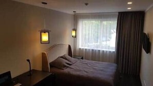 A hotel room with a bed, bedside tables, lamps, and a window with curtains.