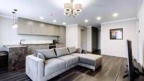 A modern living room with a sectional sofa, a flat-screen TV, and a kitchen in the background.