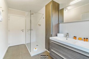 A modern bathroom with a glass-enclosed shower, a white sink, and wooden cabinetry. - Villa Zee en Zand-bungalow with garden and parking (Middelkerke)