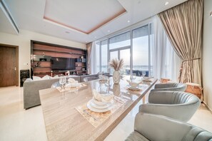 A modern dining area with a long table set for four, a sofa, and a television in the background. - Vibrant Palm Lifestyle and Mediterranean Charm (Dubai)