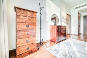 Una habitación amplia con piso de madera, un aparador grande de madera con varios cajones, un perchero y un espejo en la pared.