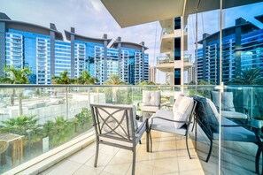 Un balcón con muebles modernos, barandilla de vidrio y vista a edificios altos.