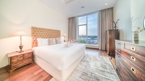 Ein Hotelzimmer mit einem großen Bett, einer Holzkommode, einem Nachttisch und Blick auf die Stadt durch das Fenster.