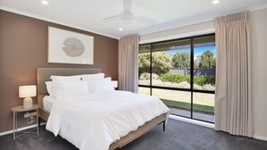 Een slaapkamer met een bed, een nachtkastje, een plafondventilator, een raam met gordijnen en een kunstwerk in een lijst aan de muur.