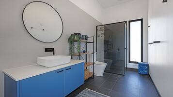 A modern bathroom with a white sink, blue cabinets, a round mirror, and a glass shower enclosure.