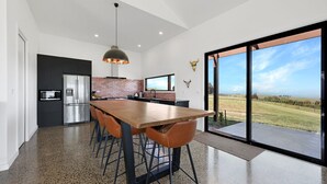 Cozinha moderna com uma mesa de jantar grande, eletrodomésticos de aço inoxidável e vista para o campo através de grandes portas deslizantes.