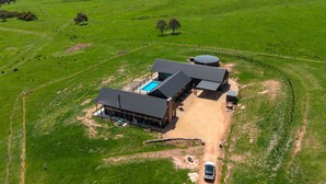 Uma grande casa de fazenda moderna com piscina, várias garagens e extensos campos verdes.