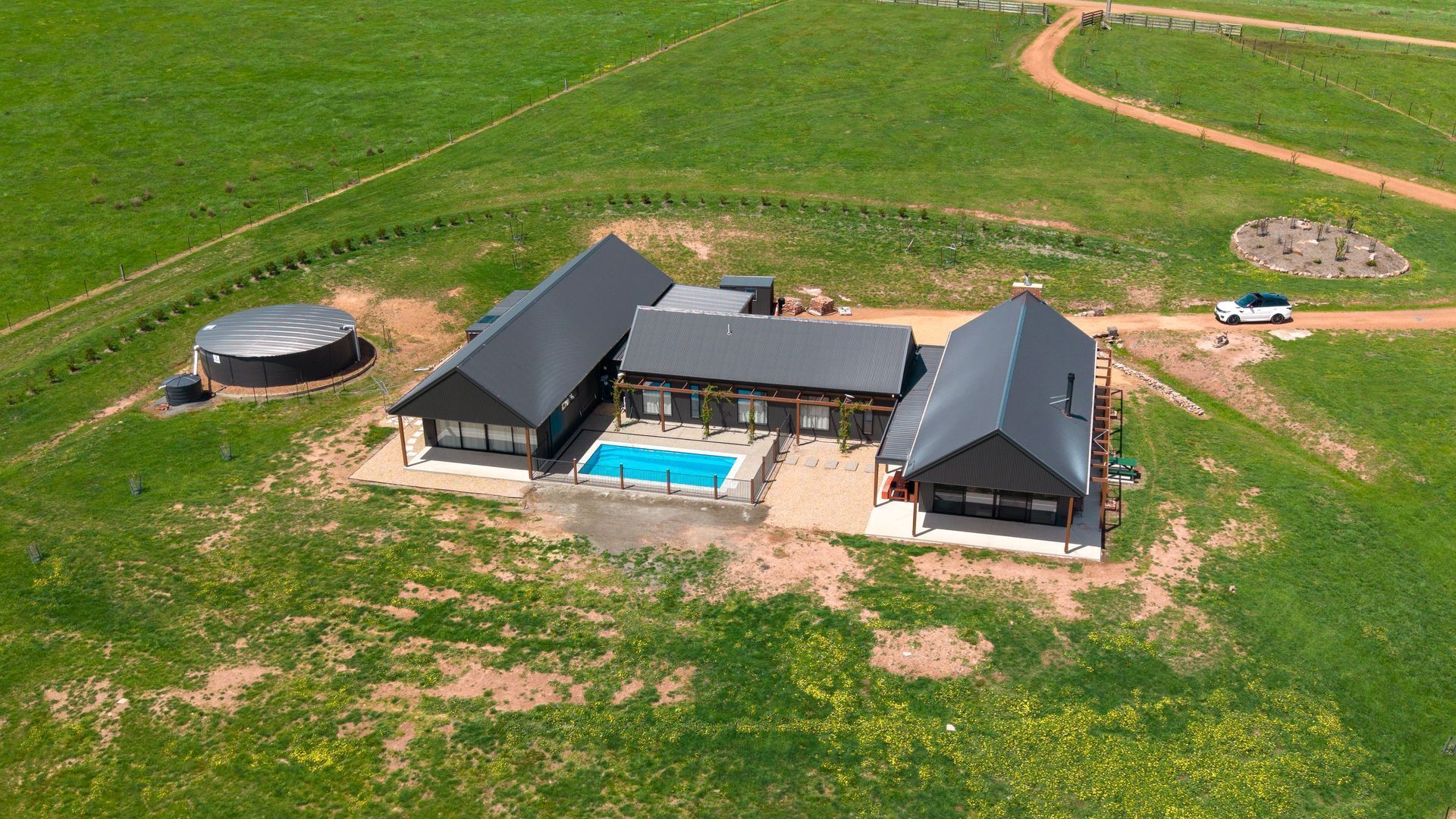 A large, modern house with a swimming pool, surrounded by a well-maintained lawn and a fenced property.